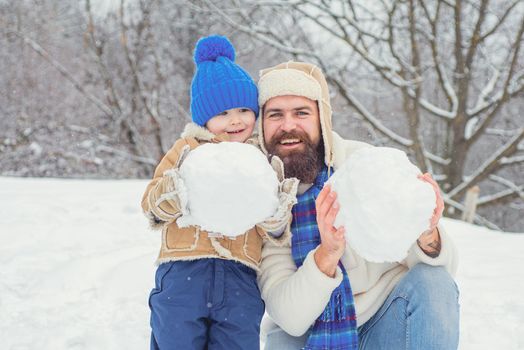 Winter, father and son play outdoor. Happy father and son making snowman in the snow.
