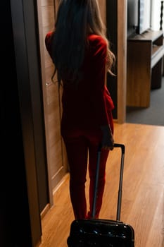 Young blond businesswoman arrives in a hotel room with black suitcase. Woman in red coral business suit.