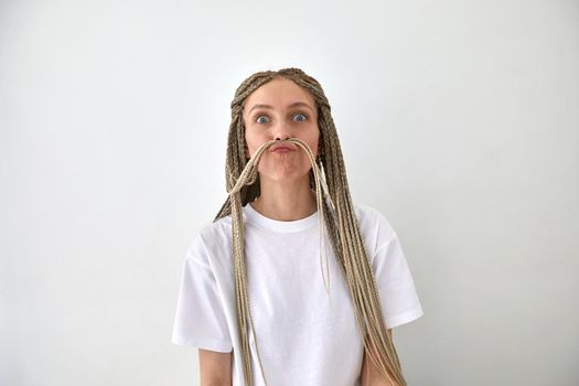 Female with long braided hair pouting lips playfully against white background and looking at camera