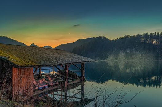 Boatshouse with a little pier in front of the alps in the sunset dawn and a little bit fog over the lake.