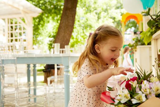 Side view of adorable little girl touching bouquet of flowers with interest in courtyard
