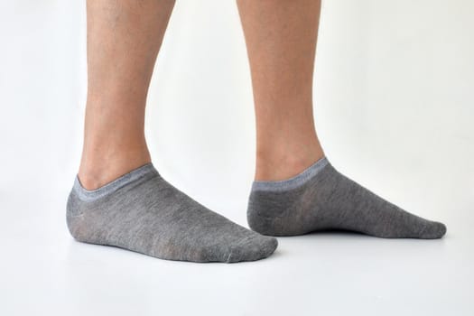 Crop anonymous male wearing gray socks standing against white background in light studio