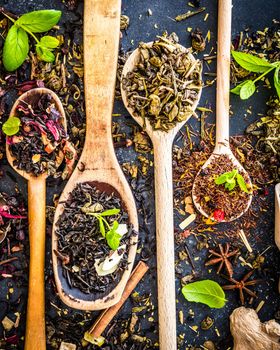 Virious kinds of tea in wooden spoons on black table