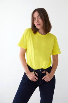 Young female model in casual bright yellow t shirt and black jeans looking at camera against white background