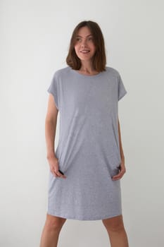 Positive female wearing cotton long sleepwear standing with hands in pockets against white background and looking away