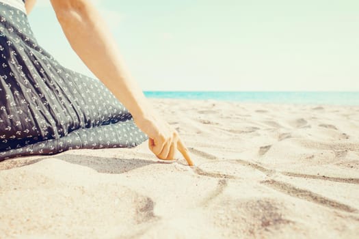 Young woman drawing on sand beach with her finger, view of hand. Sea summer vacations.