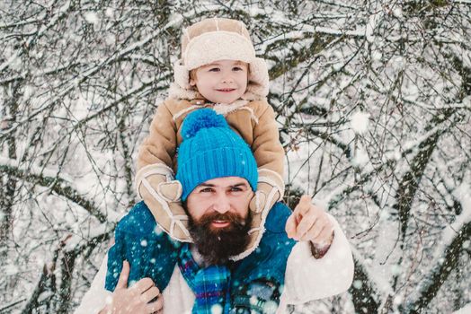 Winter, father and son play outdoor. Christmas family in snow. Merry Christmas and Happy New Year. Portrait of happy father giving son piggyback ride on his shoulders