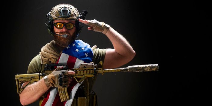 Photo of an American soldier holds a flag on his shoulder and salutes. Concept of the Day of Remembrance of Veterans.