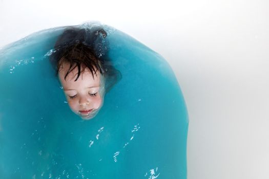 Top view of adorable little kid with closed eyes lying in bathtub with blue water and relaxing during hygiene routine