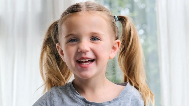 Portrait of a child with blue eyes laughs with a toothy smile. Funny little girl smiling looking at camera at home. Cute 3 years old kid preschool child with pretty face