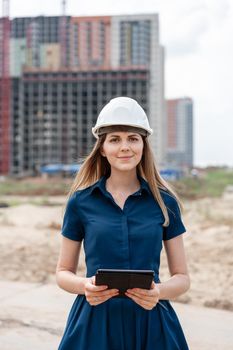 Female construction engineer. Architect with a tablet computer at a construction site. Young Woman look in camera, building site place on background. Construction concept.