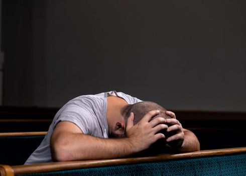 A Sad Christian man in white shirt is sitting and praying with humble heart in the church.