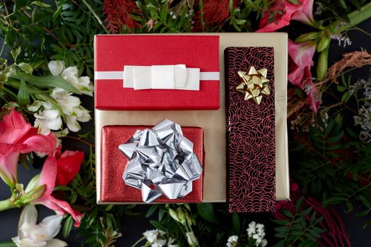 Top view composition with various elegant red colored present boxes with bows placed among blooming flowers