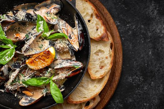 Cooked mussels in a skillet with cheese and basil leaves, on a wooden board, on a dark background