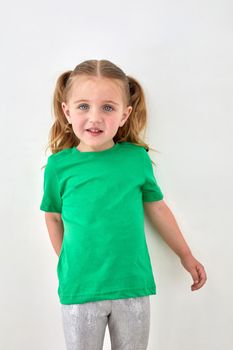 Adorable toddler girl with ponytails dressed in bright green t shirt looking at camera and smiling against white background