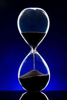 Hourglass illuminated on dark blue background close up photo