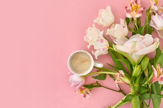 Top view of cup of fresh coffee and assorted tender flowers arranged on pink background in studio
