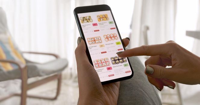 Unrecognizable woman holding phone with app delivery sushi food on screen at home