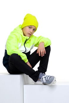 Cute stylish boy posing on staircase. Preteen boy wearing sports tracksuit with sweatshirt, pants and hat lying isolated on white background. Happy childhood, active healthy lifestyle concept