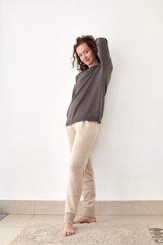 Full body of young barefoot female standing with hand behind head and smiling at camera