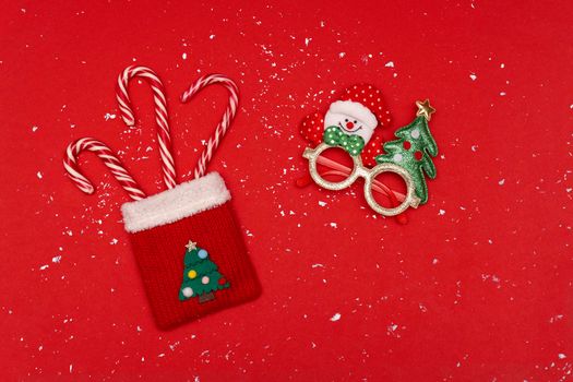 Flatlay at Christmas knitted red sack with striped candies and Christmas glasses at red Christmas background with snow flakes, Christmas and New Year conception.