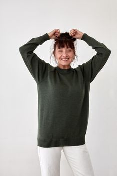Smiling middle aged female model in casual comfy woolen sweater and white pants raising hands and looking at camera