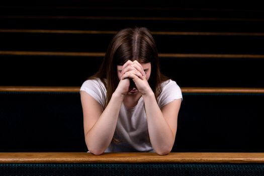 A Sad Christian girl in white shirt is sitting and praying with humble heart in the church.