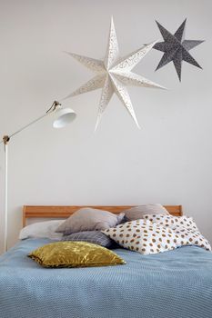 Star shaped decorations hanging over modern lamp and comfortable bed with pillows in cozy bedroom