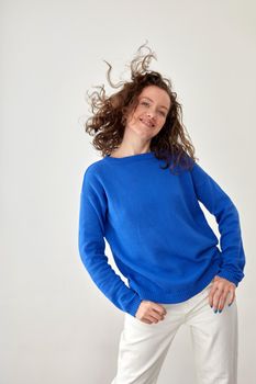 Young female model in trendy oversize blue woolen sweatshirt looking at camera against white background