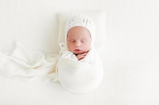 Sleeping newborn baby girl wrapped in white blanket