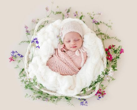 Sleeping newborn baby girl wrapped in a basket with flowers