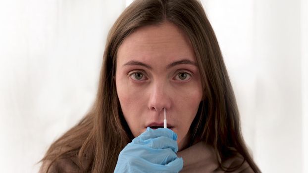 Woman with loose hair in blue surgical gloves takes swab from nasal mucosa to detect coronavirus infection using medical tampon