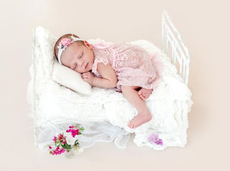 Sleeping newborn baby girl in a pink dress in a small crib