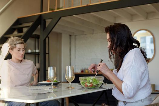 Side view of young female serving salad from bowl while having romantic dinner with girlfriend at home