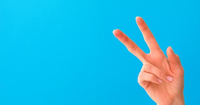 Close up of beautiful female hand doing victory sign, isolated on blue studio background with copy space for adversminted. Body Language concept. Hand sign