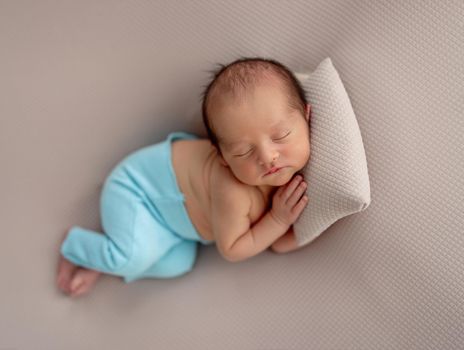 Cute newborn in blue pants sleeping on tiny pillow