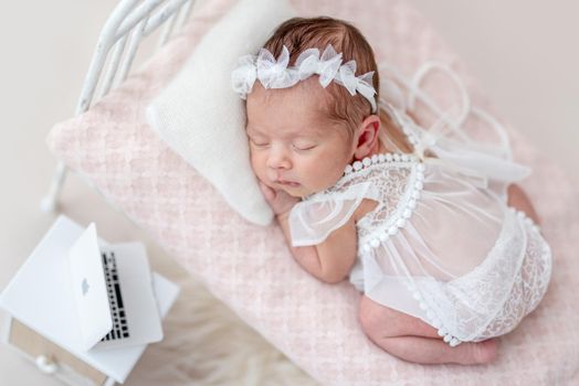 Cute asleep newborn on tiny bed with a laptop on the nightstand
