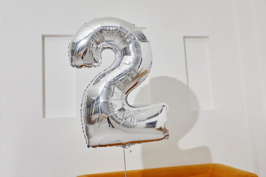 Silver foil balloon in shape of number two during birthday celebration against white wall