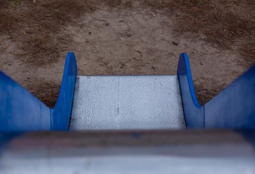 Children's slide with blue sides and a shiny metal surface. Top down view of children's slide.