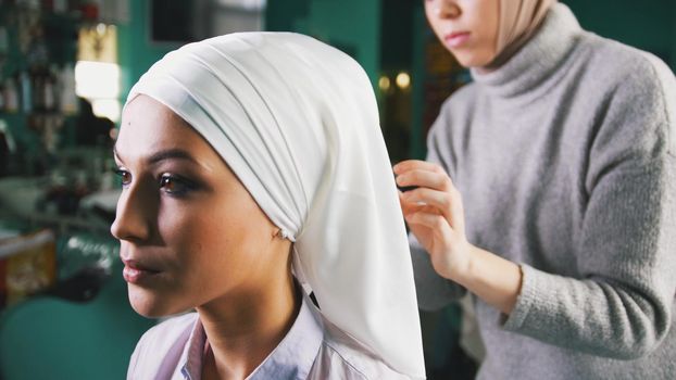 Muslim woman in the background makes Islamic turban for beautiful bride, close up