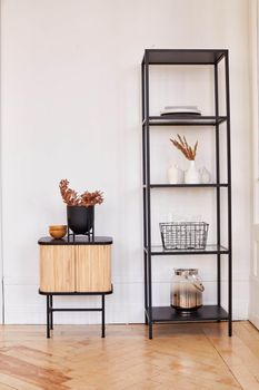 Modern metal shelves and wooden cabinet with assorted decorations placed in room in minimal style