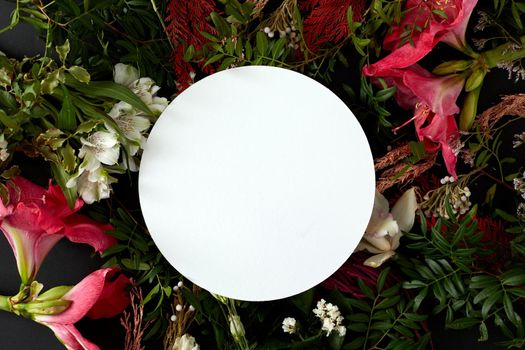 Top view composition with various fresh blooming flowers with green foliage arranged around blank white round plate
