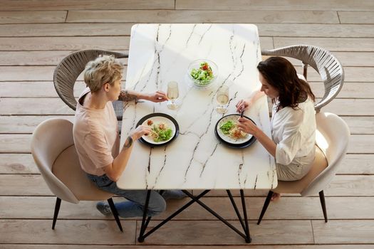 Couple enjoying dinner meal sitting at kitchen table together and drinking white wine, healthy eating view from above