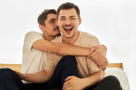 Cute male gay couple hugging and looking at the camera at home isolated