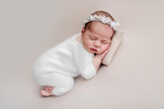 Newborn in knitted white suit and diadem sleeping on pillow