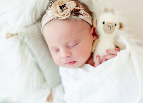 Sleeping newborn baby girl wrapped in white blanket in a small crib