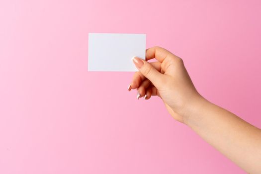 Woman hand showing blank business card on pink background. Close up.