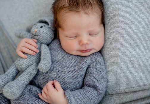 Newborn baby boy wearing in knitted costume sleeping and holding toy bunny. Infant kid studio portrait with decoration