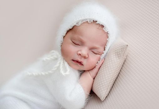 Newborn in knitted white suit and diadem sleeping on pillow