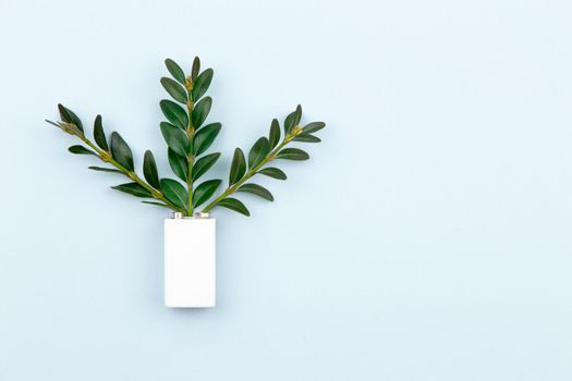 Eco energy or green power illustration with a white battery and sprigs leaves on a light background with copy space for text